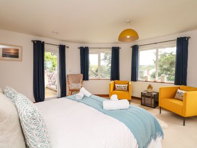 A bedroom with a bed a blue blanket two yellow chairs and blue curtains at Nairn in Braunton