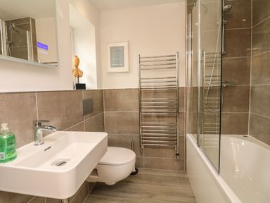 A bathroom with a wall-mounted toilet sink and bathtub with glass shower at Nairn in Braunton