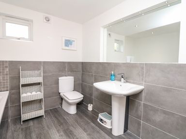 A bathroom with a toilet a sink a large mirror a small window and a white storage rack with towels at Nairn in Braunton