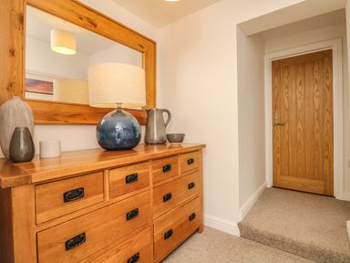 A hallway with a wooden dresser with black handles a large wooden framed mirror and decorative items next to a wooden door at Nairn in Braunton