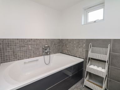 A bathroom with a white bathtub tiled walls and a wicker storage rack with towels at Nairn in Braunton