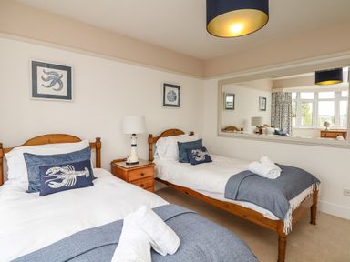 A bedroom with two single beds with blue and white bedding and a wooden nightstand with a lamp at Nairn in Braunton