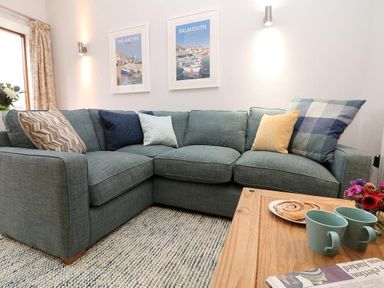 A living room with a sectional sofa with cushions a wooden table with two mugs and pastries at Hazel Barn in Falmouth