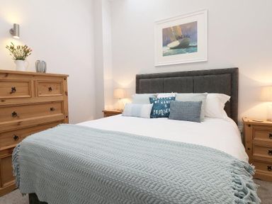 A bedroom with a bed with pillows and a blue throw blanket wooden dressers and a framed picture of a sailboat on the wall at Hazel Barn in Falmouth