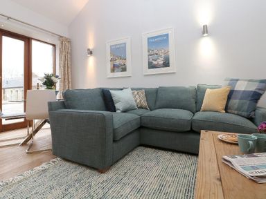 A living room with a blue sectional sofa several cushions a wooden coffee table with cups and a plate and wall art at Hazel Barn in Falmouth