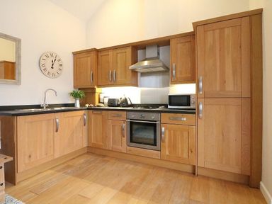 A kitchen with wooden cabinets a built-in oven a microwave a sink and a wall clock at Hazel Barn in Falmouth