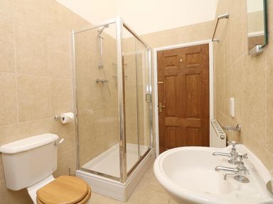 A bathroom with a shower enclosure a toilet with a wooden seat and a white sink with faucets at Hazel Barn in Falmouth