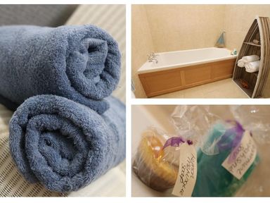 Rolled blue towels on a surface bathtub with wooden panel and boat-shaped shelf with towels and decorations wrapped soap bars with tags