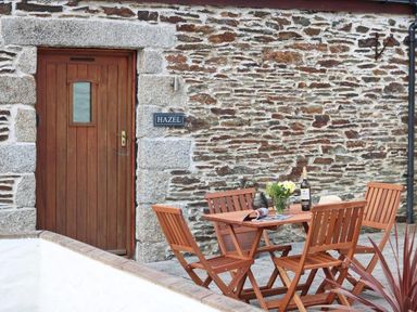 An outdoor seating area with wooden table and chairs against a stone wall with a wooden door and a sign that reads Hazel at Hazel Barn in Falmouth