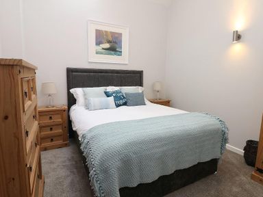 A bedroom with a bed with multiple pillows and a blue blanket a wooden dresser and nightstands with lamps at Hazel Barn in Falmouth
