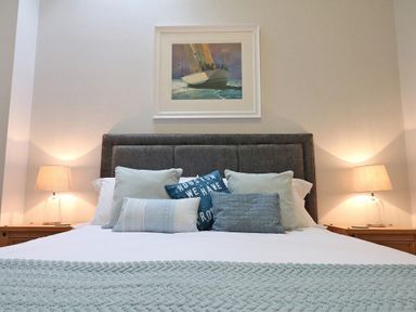 A bedroom with a bed with multiple pillows and two bedside tables with lamps and a painting of a boat on the wall above the headboard at Hazel Barn in Falmouth