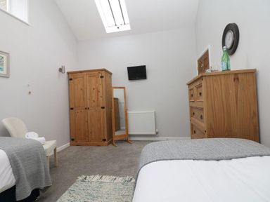 A bedroom with two single beds wooden wardrobe wooden dresser wall-mounted TV and a chair at Hazel Barn in Falmouth
