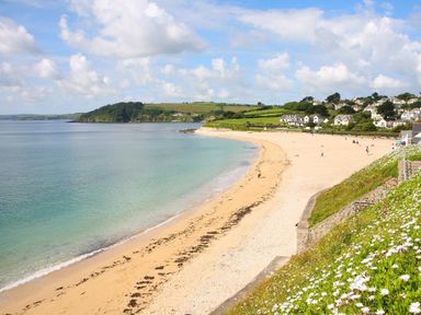 A beach with clear water and sand near houses and green hills at Hazel Barn in Falmouth