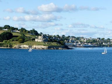 A coastal view with blue water sailboats and a stone building on a grassy hill at Hazel Barn in Falmouth