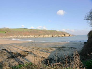 A sandy beach with seaweed and waves by a rocky coastline with grassy hills at Hazel Barn in Falmouth