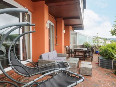 An outdoor patio with a hanging chair two-seater sofa a glass coffee table dining table with chairs and plants at Bight Boathouse in Dartmouth