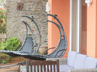 A patio with two hanging chairs and a cushioned wicker sofa at Bight Boathouse in Dartmouth