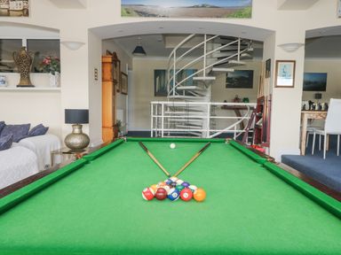 A room with a pool table with balls and cues a spiral staircase and seating areas at Bight Boathouse in Dartmouth