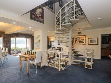 A room with a spiral staircase a chess table and large windows overlooking water at Bight Boathouse in Dartmouth