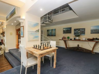 A room with a chess table and two white chairs a wooden console table with decorations spiral staircase and paintings on the wall at Bight Boathouse Dartmouth