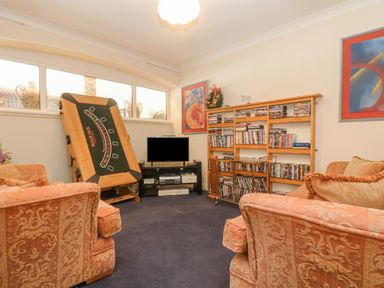 A den with two armchairs a blackjack table a television on a stand and a wooden bookshelf filled with books and DVDs at Bight Boathouse in Dartmouth