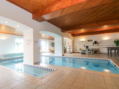 An indoor swimming pool area with exercise equipment and a seating area at Bight Boathouse in Dartmouth