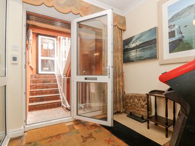 An entryway with an open glass door leading to stairs outside and wall art above a carved stone and a small wooden shelf at Bight Boathouse in Dartmouth