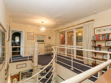 An upper floor landing with a spiral staircase bookshelves paintings and framed pictures at Bight Boathouse in Dartmouth