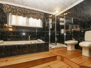 A bathroom with a bathtub a shower a bidet and a toilet with dark tiles on the walls and wooden flooring at Bight Boathouse in Dartmouth