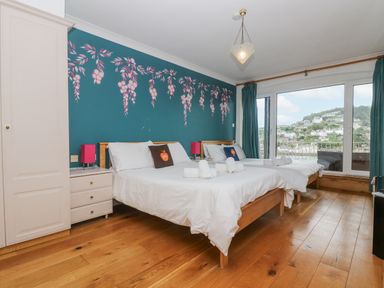 A bedroom with two beds wooden floor a wardrobe and large windows overlooking a hillside at Bight Boathouse in Dartmouth
