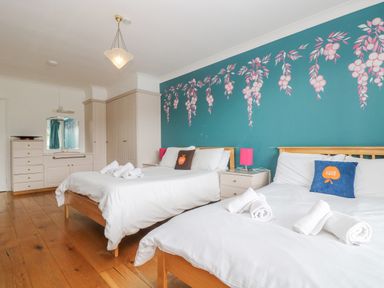 A bedroom with two beds white linens wooden floors and teal wall with floral design at Bight Boathouse Dartmouth