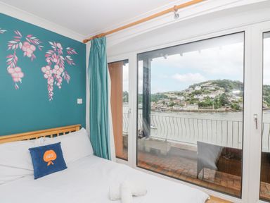A bedroom with a bed and pillow next to a large window with a view of a river and hillside at Bight Boathouse in Dartmouth