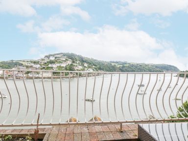 A balcony overlooking a body of water with boats and a hillside with houses at Bight Boathouse in Dartmouth