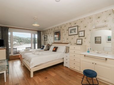 A bedroom with two beds a dresser a vanity with a mirror and stool and a large window overlooking water at Bight Boathouse in Dartmouth