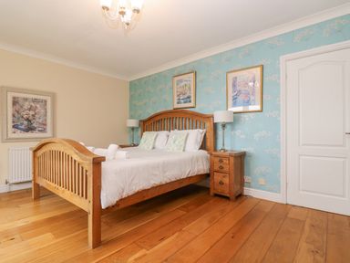 A bedroom with a wooden bed and bedside tables with lamps and framed pictures on the wall at Bight Boathouse in Dartmouth