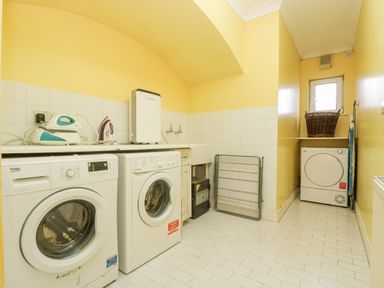 A laundry room with washing machines a dryer an ironing board and a laundry basket at Bight Boathouse in Dartmouth
