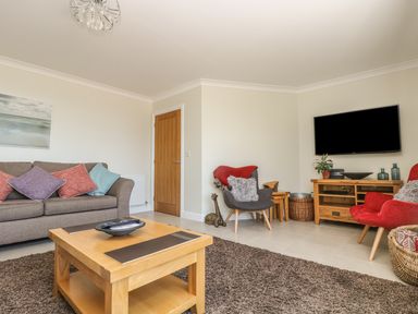 A living room with a sofa with cushions a wooden coffee table armchairs and a wall-mounted TV at Hagar Vor in Marazion