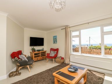 A living room with two chairs a wooden coffee table and a television mounted on the wall at Hagar Vor in Marazion