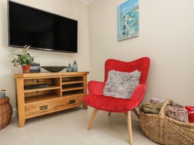 A red armchair with a gray pillow next to a wooden media console with a television mounted above at Hagar Vor in Marazion