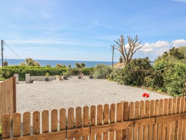 A fenced gravel yard with plants and a view of the sea at Hagar Vor in Marazion