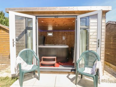 An outdoor seating area with two plastic chairs and an open wooden shed containing a hot tub at Hagar Vor in Marazion