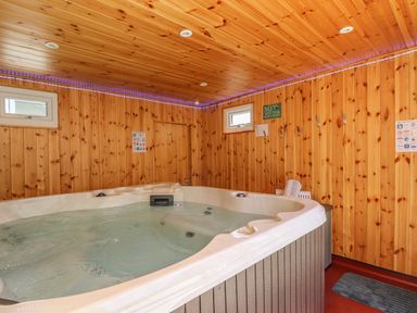 An indoor hot tub with wooden walls and ceiling and small windows at Hagar Vor in Marazion