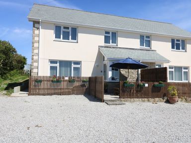 A two-story house with multiple windows a gated patio with a blue umbrella and flower boxes on the fence at Hagar Vor in Marazion