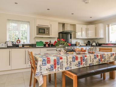 A kitchen with white cabinets a dining table with a printed tablecloth and chairs at Hagar Vor in Marazion