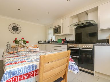 A kitchen with a table covered by a printed tablecloth with red roses eggs and bread on it and a stove and microwave in the background at Hagar Vor in Marazion