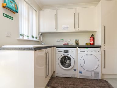 A laundry room with a washing machine dryer fire extinguisher first aid kit and cabinets at Hagar Vor in Marazion