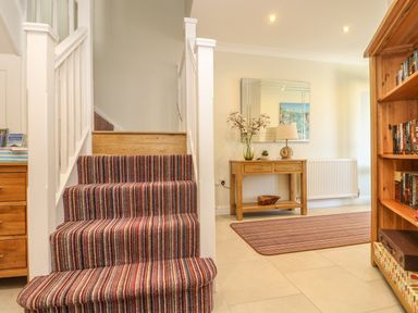 A hallway with stairs covered in striped carpet next to a wooden console table with decorations and a mirror above at Hagar Vor in Marazion
