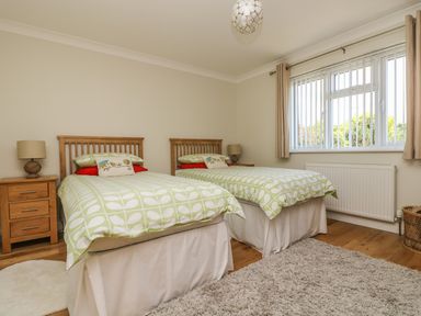 A bedroom with two single beds green patterned bedding wooden headboards bedside tables with lamps a window with vertical blinds and a beige rug on a wooden floor at Hagar Vor in Marazion