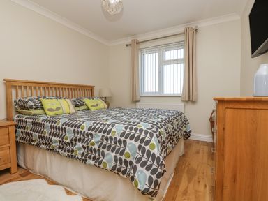A bedroom with a double bed covered with patterned bedding two bedside tables a window with blinds and curtains a wooden floor and a dresser with a vase at Hagar Vor Marazion