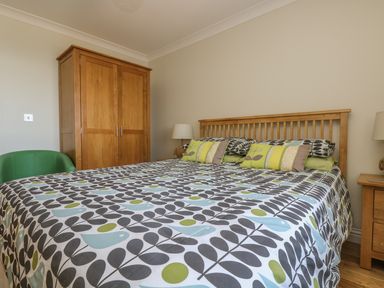 A bedroom with a patterned bedspread wooden wardrobe green chair and wooden bedside tables with lamps at Hagar Vor in Marazion